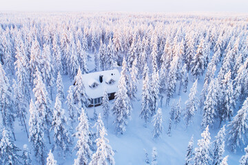 An aerial view of small wooden cabin in the middle of winter wonderland in a wintery and cold taiga forest, Northern FInland. 