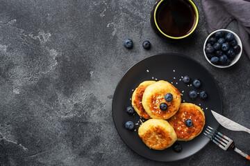 Fritters of cottage cheese with blueberries. Cheese curd cheesecakes, pancakes on a dark concrete background. Copy space.