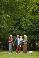 Fototapeta premium Vertical wide angle portrait of carefree family with two kids and pet dog standing on green grass outdoors while enjoying walk in park together, copy space