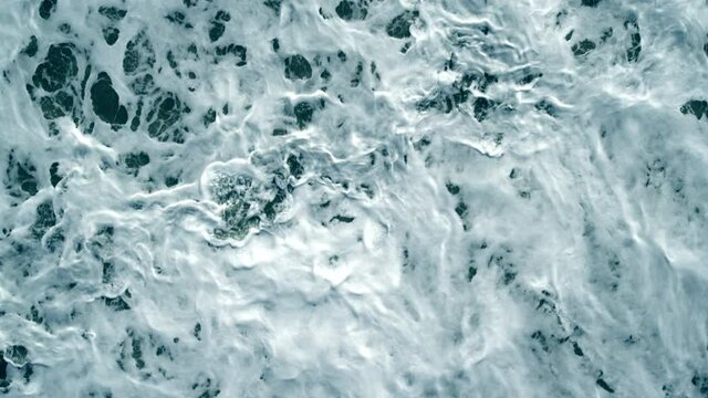 View from Top over coastal storm waves. Drone Topdown with blue waves and white foam. Empty aerial wide shot with no people.