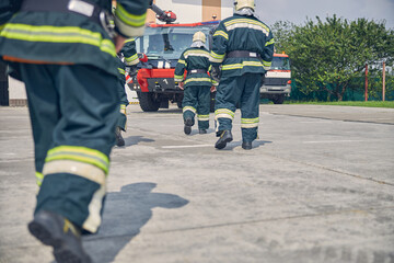 Three confident strong men running to modern truck at fire station