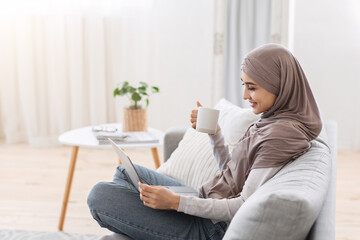 Domestic Lifestyle. Muslim Woman Relaxing At Home With Laptop And Drinking Coffee