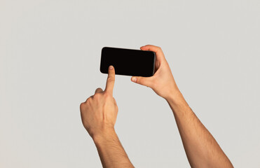 Unrecognizable millennial man touching screen of cellphone over light background, space for mobile app design