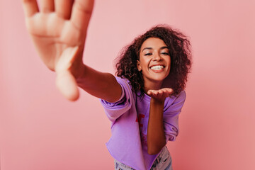 Adorable funny woman sending air kiss. Charming african girl making selfie with inspired face expression.