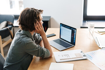 Image of young focused woman working with laptop while sitting at table