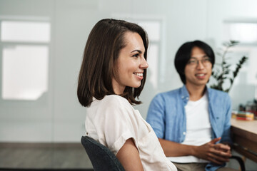 Image of young smiling colleagues discussing project while working