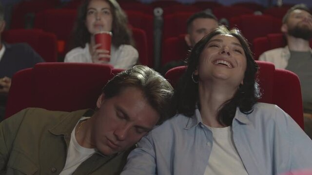 Medium shot of pretty Caucasian woman is enjoying movie in the cinema while her boyfriend is sleeping on her shoulder