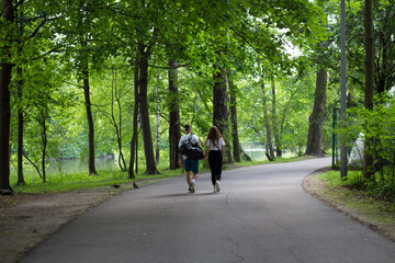 Fototapeta premium A happy young couple in sports clothes walk hand in hand along the path of the Park on a summer day.