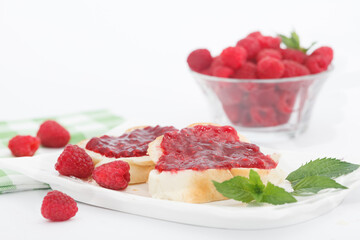 Raspberry jam with fresh raspberries and bread slices on white plate. Homemade marmalade, perfect for light, sweet breakfast.