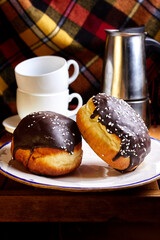 Two donuts in chocolate glaze near cups and geyser coffee maker