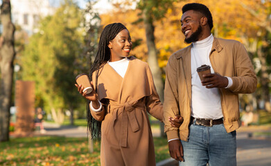Millennial afro couple walking in autumn park and drinking takeout coffee