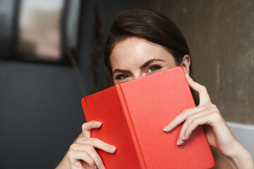 Image of joyful woman putting diary over her face and looking at camera