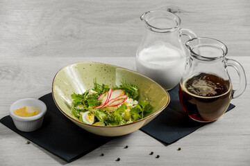 Vegetable okroshka with adyghe cheese (traditional Russian summer cold soup) and two jugs with kvass and kefir are on a wooden background.