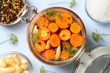 Healthy vegan food. Homemade fermented carrots with garlic, dill and pepper in a glass jar. Light blue background. Top view, close-up.