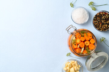 Healthy vegan food. Homemade fermented carrots with garlic, dill and pepper in a glass jar. Light blue concrete background. Top view, space for text.