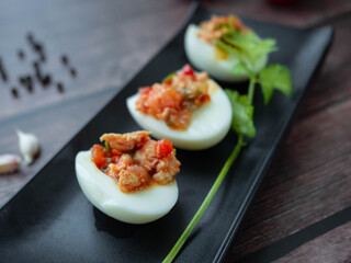 Stuffed Eggs with minced pork
Tomato,Onions,Garlic,Pepper stir well,Place the filling on a boiled egg on a Black plate,Background wood Boiled eggs