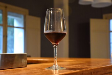 Glass cup with aged red wine on a wooden bar counter.