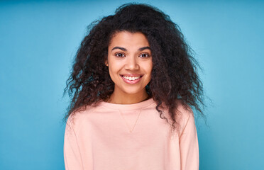 Fototapeta premium Portrait of an attractive smiling curly dark-skinned lady on a blue background.