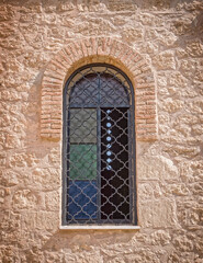 Fototapeta na wymiar old arched window secured with iron grid on rough stone wall