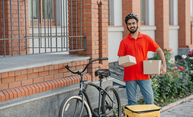 Obraz premium Fast delivery for many online purchases. Smiling courier with beard holds cardboard boxes