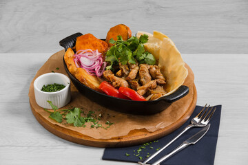 Saj with chicken (Georgian dish with tender chicken meat in aromatic spices with baked vegetables and homemade grilled flatbread) and fork, knife are on the white wooden background.