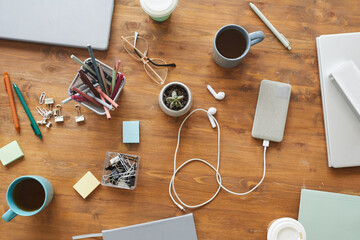 Top view background image of cluttered workplace table with cups, mugs and stationary items, teamworking or studying concept, copy space