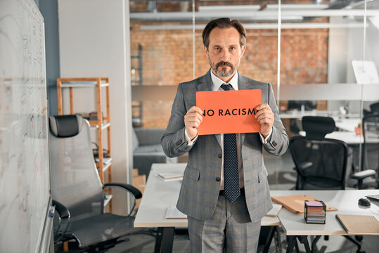 Serious Man Standing In Office And Holding No Racism Placard