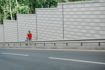 Delivery route. Courier in helmet, with yellow backpack and bicycle walks along the track on street to client