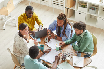 High angle view at contemporary creative team working together at cluttered table with mugs and stationary items, teamworking or studying concept, copy space