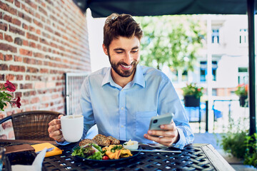 Young entrepreneur eating breakfast and looking at smartphone