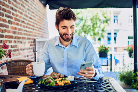 Young entrepreneur eating breakfast and looking at smartphone