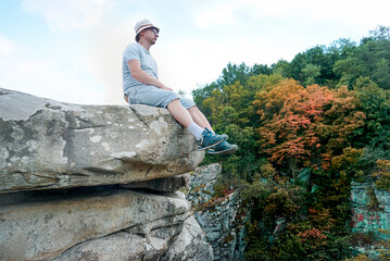 Naklejka premium A guy sits on a rock in the mountains on a stone, dressed in a T-shirt and shorts