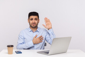 I swear! Honest businessman sitting office workplace with laptop on desk, raising hand, touching chest and making sincere promise, looking trustworthy reliable. studio shot isolated, white background
