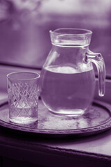 Jug of water and a glass on the windowsill, violet tone.
