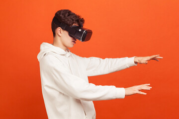 Concentrated self confident teenager in white casual hoodie moving with vr headset on eyes, online...