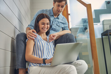Pretty smiling lady with handsome man watching something on the laptop