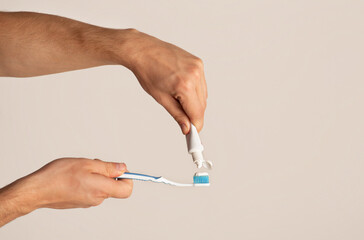 Dental hygiene. Young guy applying paste from tube onto toothbrush against light background, copy space