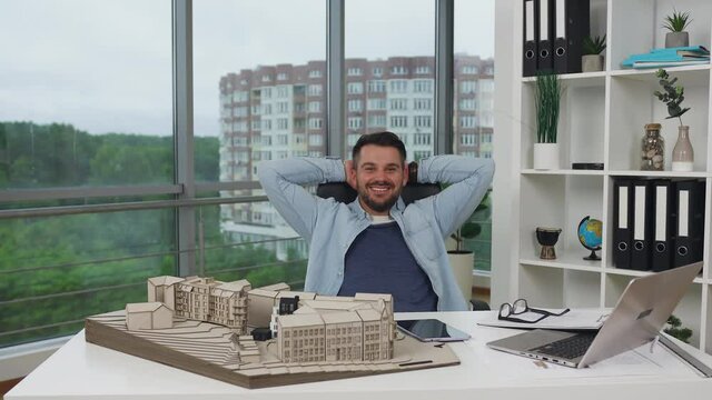 Good-looking joyful contented smart bearded male designer posing in beautifully designeted architectural bureau on the panoramic windows background,4k