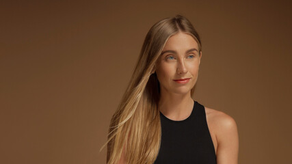 surf style looking blonde girl with hair blowing looking aside in-studio on brown