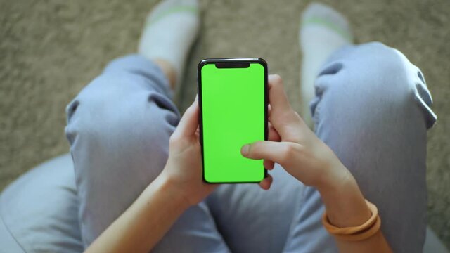 At home hands girl sitting on a couch use phone with vertical green screen smartphone chroma key communication mockup technology touchscreen social network slow motion