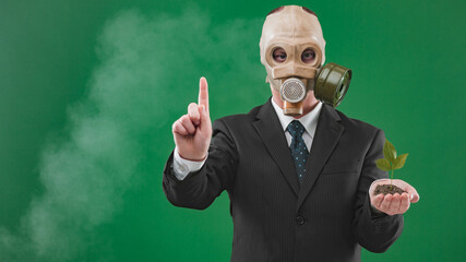 Portrait of a man wearing a dark business suit and a gas mask while holding a green plant and showing one finger, isolated on green background.