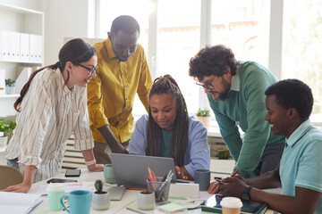 Portrait of contemporary multi-ethnic team leaning over laptop and smiling while working together in office, copy space - Powered by Adobe