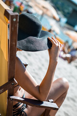 Selective focus on a black hat on a young attractive woman. She is sitting in a yellow deck chair...