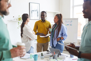 Multi-ethnic group of creative business people chatting during break in conference room, focus on smiling African-American man talking to women dressed in casual wear, copy space