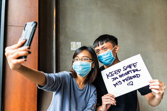Asian couple wearing a medical mask using smart phone video call conference camera and talking with their friend for keep safe during COVID-19.
