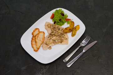 Stewed mushrooms with fish fillet, salad, fried potatoes and croutons, on a warm gray background. Tasty traditional italian food