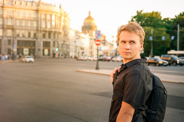Obraz premium A young blond man walks along the Palace square in the summer evening with a view of St. Isaac's Cathedral in St. Petersburg
