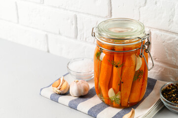 Healthy fermented food. Homemade fermented carrots with garlic, dill and pepper in a glass jar. Light background. Copy space.