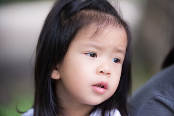 Preschool child girl keeps food on her cheeks. The little Asian daughter looked at the camera and smiles a little. Kid 3 years old. Close up shot.