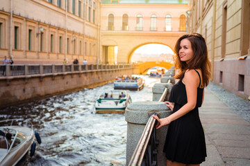 Fototapeta na wymiar A pretty girl walks through the summer of St. Petersburg and stopped on the embankment, along the channels of which excursion boats go. Russian tourism